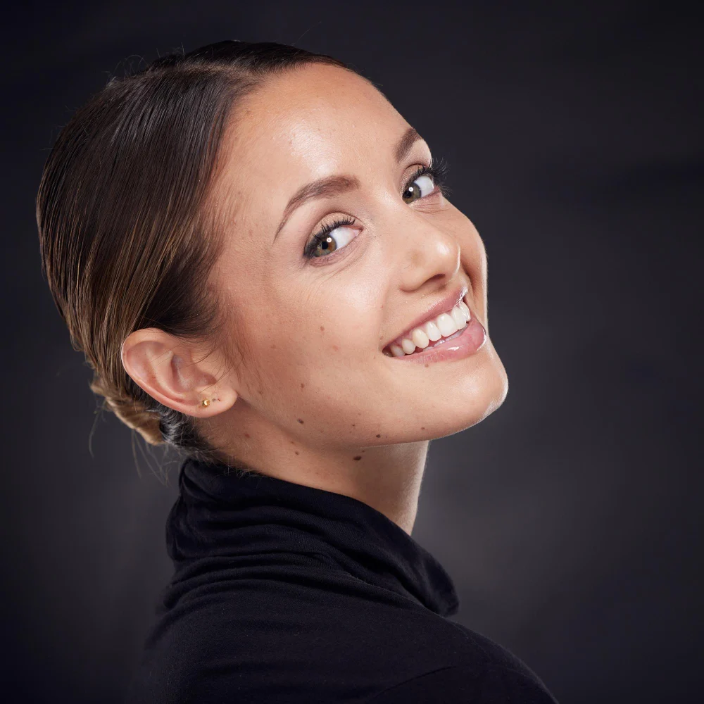 Side view of young woman smiling on dark background