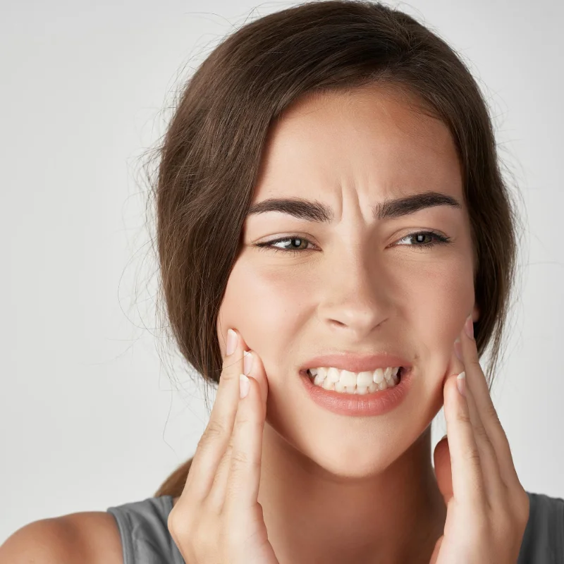 Young woman holding her cheeks, experiencing jaw pain